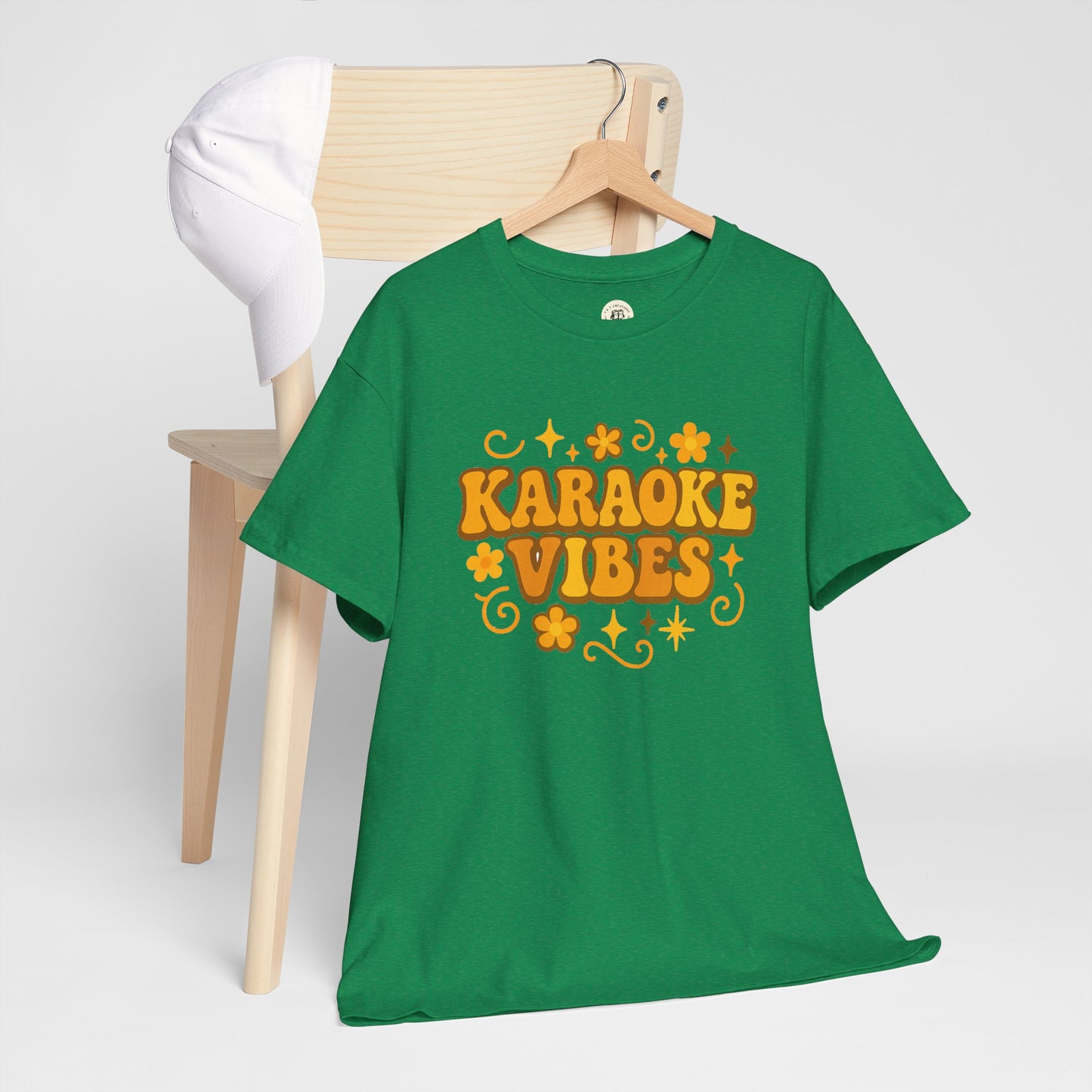 Green karaoke vibes t-shirt with orange retro text and floral design hanging on wooden chair with white cap