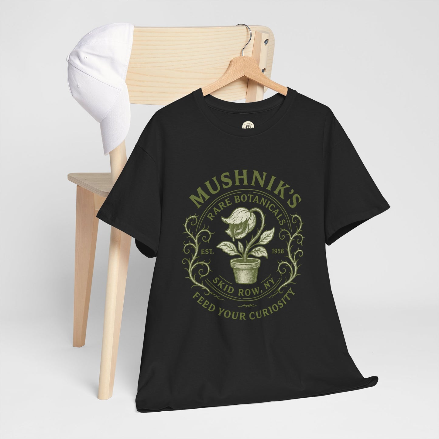 Black Little Shop of Horrors t-shirt featuring Mushnik's Rare Botanicals design hanging on wooden chair with white cap