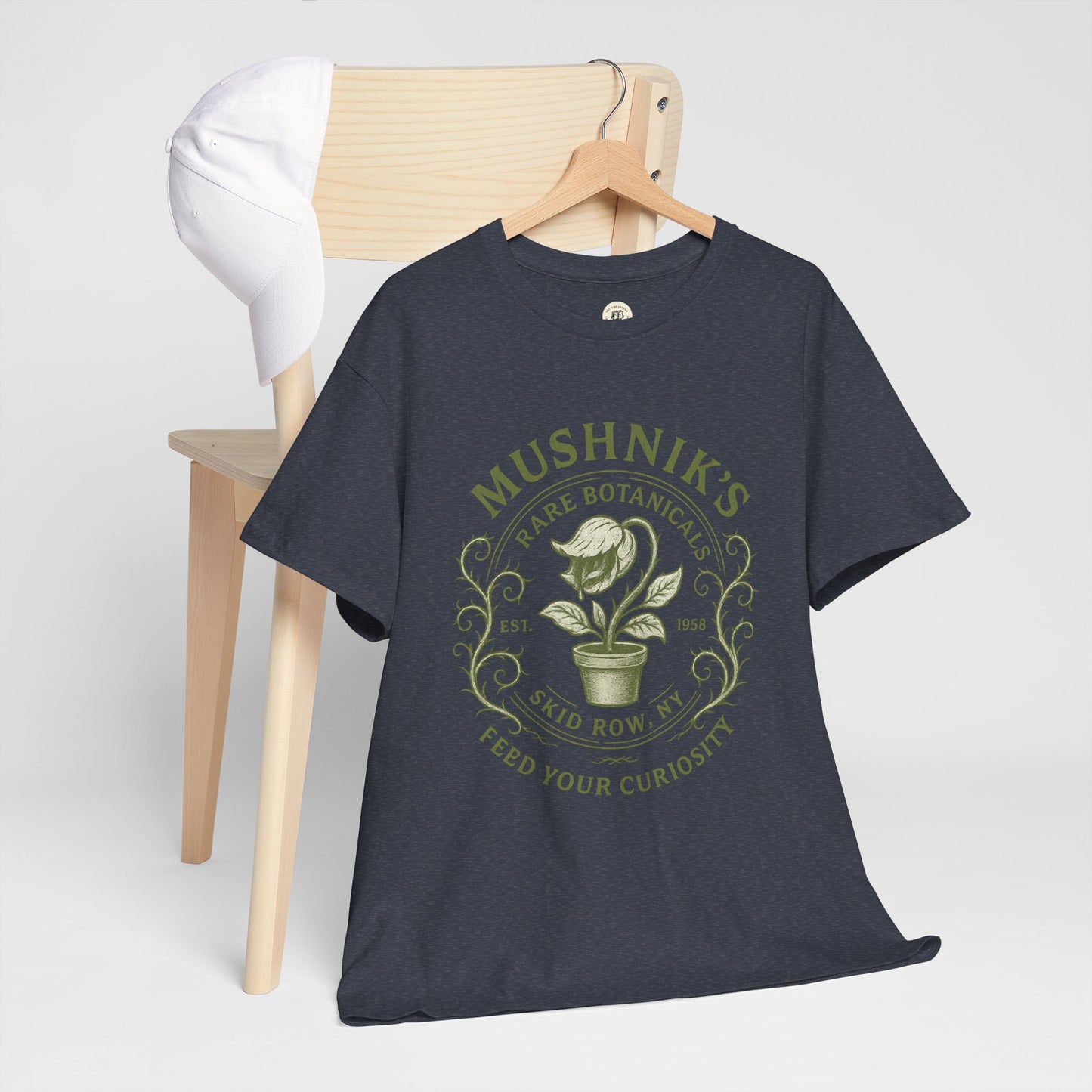 Printify Little Shop of Horrors t-shirt with green botanical graphic on black fabric hanging on wooden chair