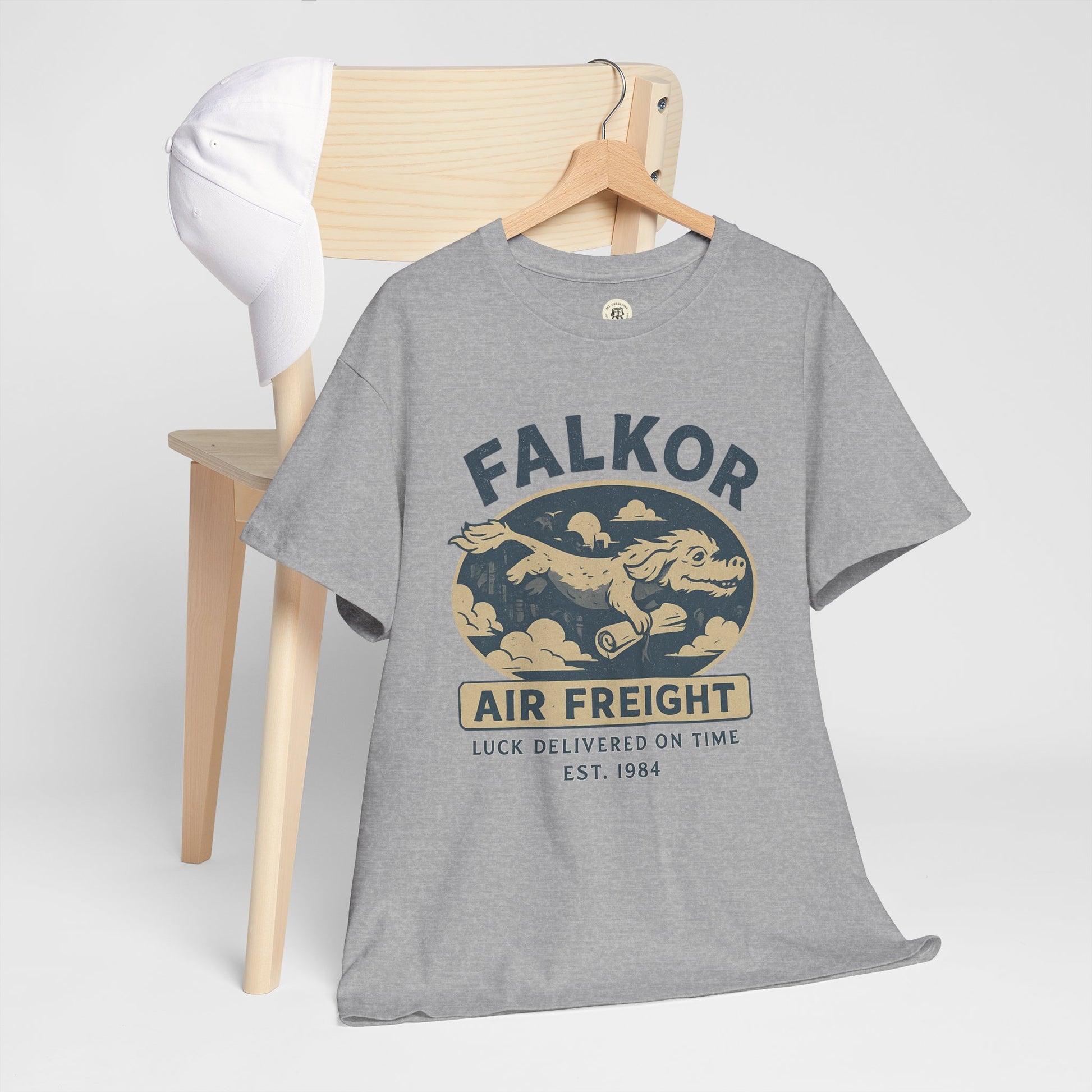 Gray Falkor Neverending Story t-shirt with air freight design on wooden chair and white cap